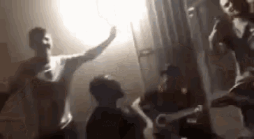 a group of people are dancing in a dark room with a light shining through the window .