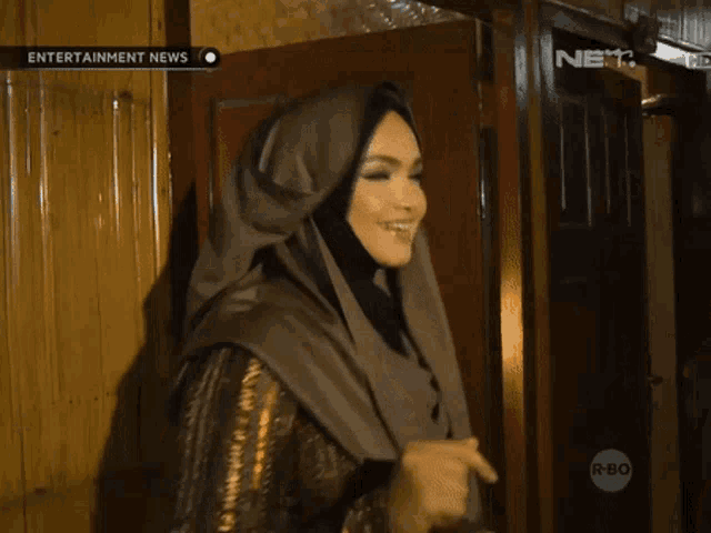 a woman in a hijab is waving in front of a door that says entertainment news on it