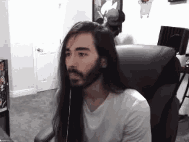 a man with long hair and a beard is sitting in a chair wearing headphones .