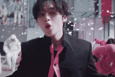 a man in a black suit with a pink tie is standing in front of a group of people