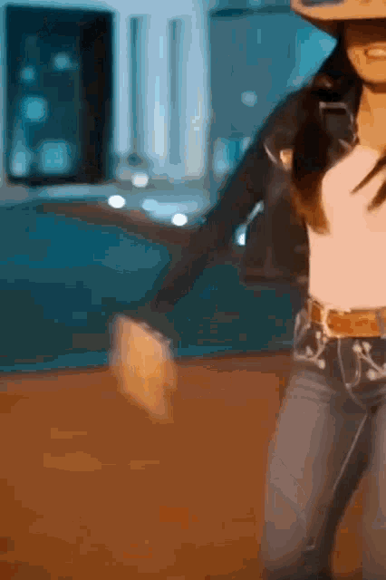 a woman wearing a cowboy hat and jeans is dancing on a stage .