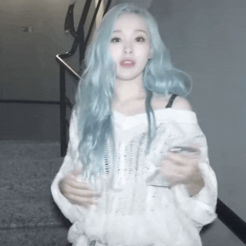 a woman with blue hair is wearing a white sweater and holding a cell phone .