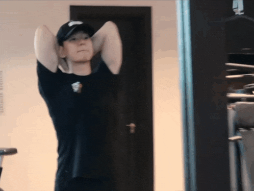 a man wearing a black shirt and a black hat is stretching his arms in front of a door