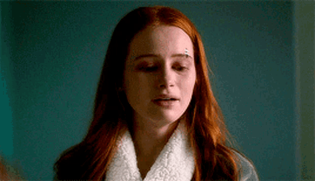 a woman with red hair is wearing a white robe and has a bandage on her eyebrow .