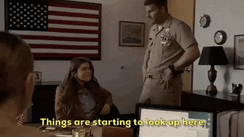 a man in a military uniform is standing next to a woman sitting at a desk in a room .