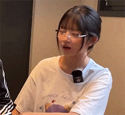 a young woman wearing glasses and a white shirt is sitting at a table .