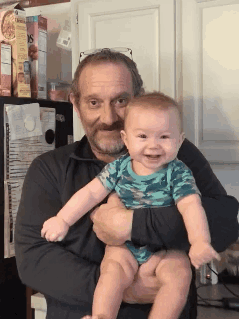 a man holds a baby in his arms in front of a box of granola bars