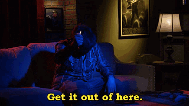 a man sitting on a couch with the words " get it out of here " behind him