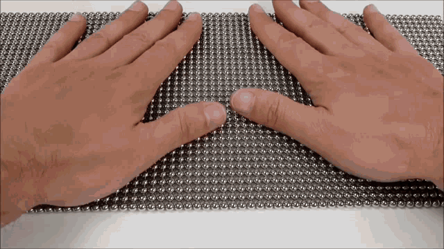 a person 's hands are playing with a grid of metal beads