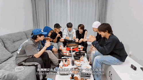 a group of young men are sitting around a table eating food and talking