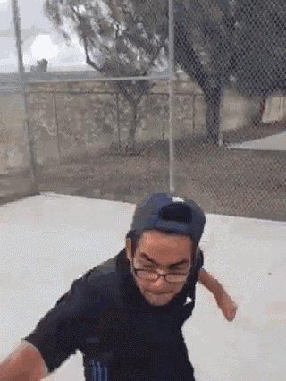 a man wearing glasses and a hat is standing in front of a chain link fence .