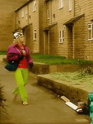 a woman in a purple jacket and neon green pants walks down a sidewalk