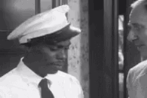 a man in a hat and tie is talking to another man in a suit .