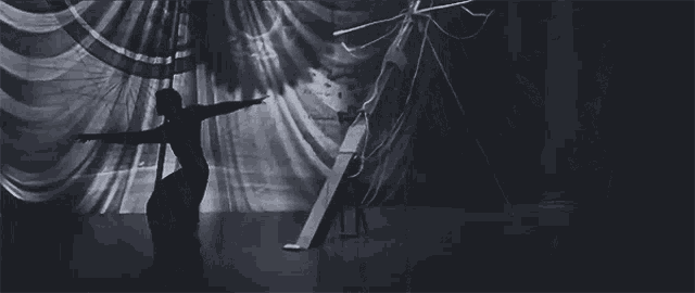a black and white photo of a person standing in front of a curtain with a map of the world projected on it