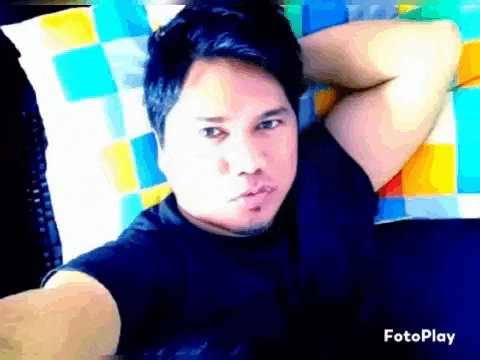 a man in a black shirt is laying on a bed with his hands behind his head and the word fotoplay on the bottom right