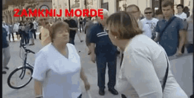 two women are standing next to each other on a street with the words zamknij morde written in red