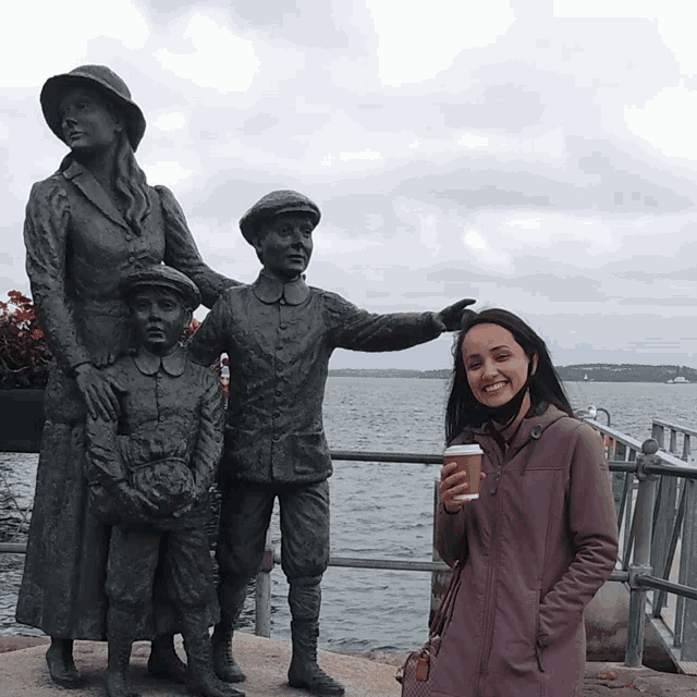 a woman is standing in front of a statue of a family holding a cup of coffee