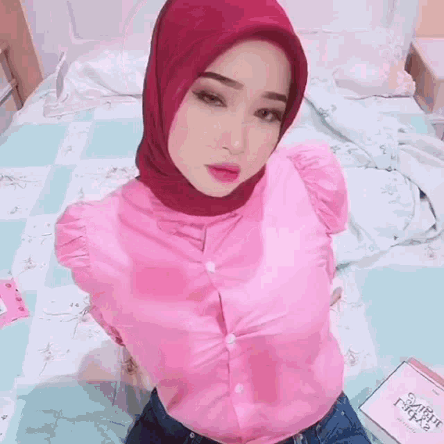a woman in a pink shirt and red hijab is holding a box .