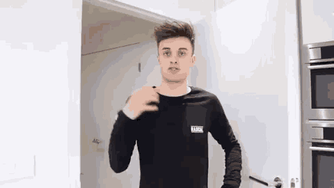 a young man is standing in a kitchen wearing a black sweatshirt .