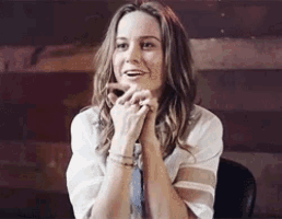 a woman in a white shirt is smiling with her hands folded in front of her face