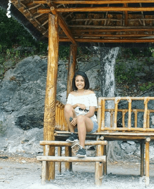 a woman sits on a wooden bench under a wooden gazebo
