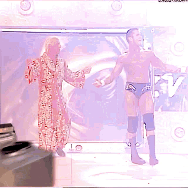 a man in a robe stands next to a shirtless man in black trunks