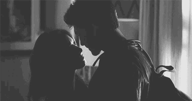 a black and white photo of a man and woman kissing in a room .