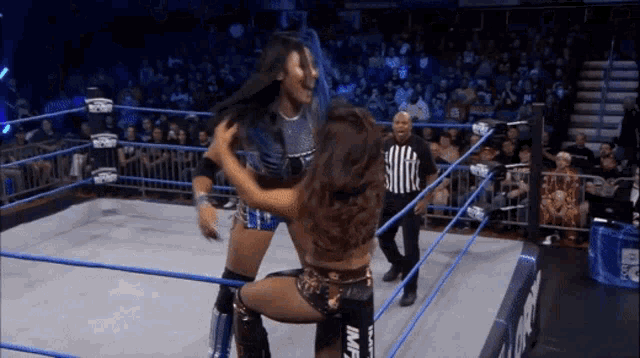 two women are wrestling in a ring with a referee standing behind them