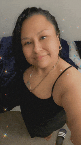 a woman in a black tank top is taking a selfie in front of a bed