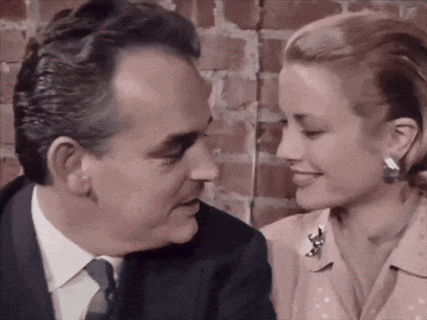 a man in a suit and tie is kissing a woman in a pink shirt .