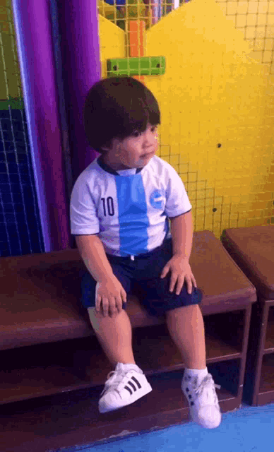 a little boy wearing a shirt with the number 10 on it sits on a bench