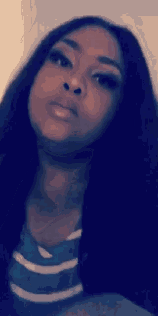 a woman with long black hair and a striped shirt is looking at the camera .