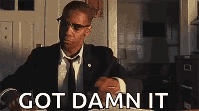 a man in a suit and tie is sitting at a table with the words `` got damn it '' written on the screen .