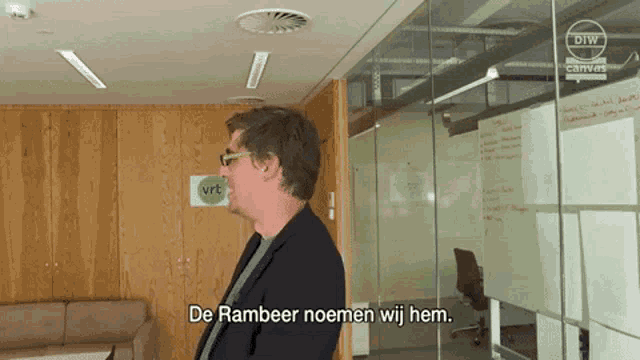 a man wearing sunglasses stands in front of a sign that says ' de rambeer noemen wij hem '