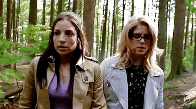 two women are walking through the woods together and one is wearing glasses .