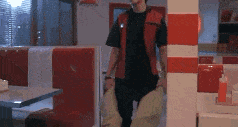 a man in a red vest is standing in a diner with red and white striped walls .