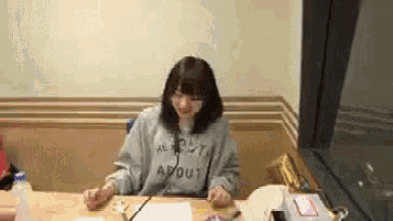 a woman is sitting at a table wearing a sweatshirt that says about