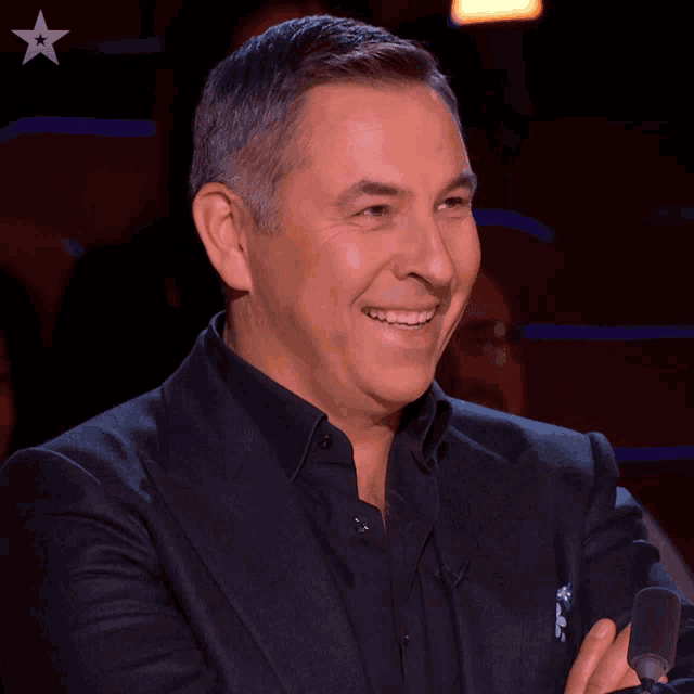a man in a suit is smiling and holding a microphone with a star in the background