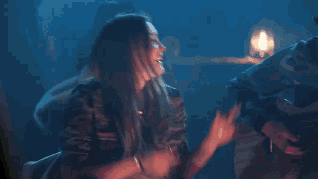 a woman is laughing while sitting in a dark room with a candle in the background