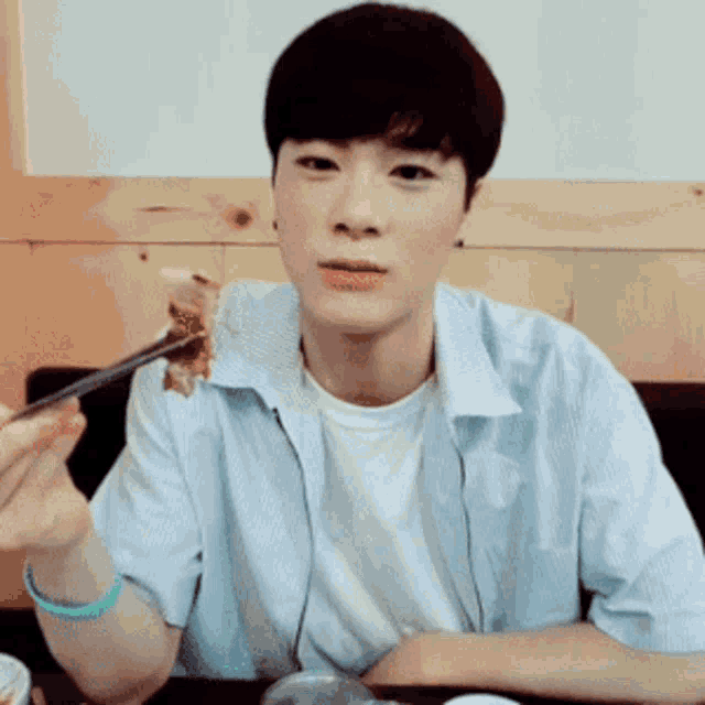 a young man is sitting at a table eating a piece of food with chopsticks