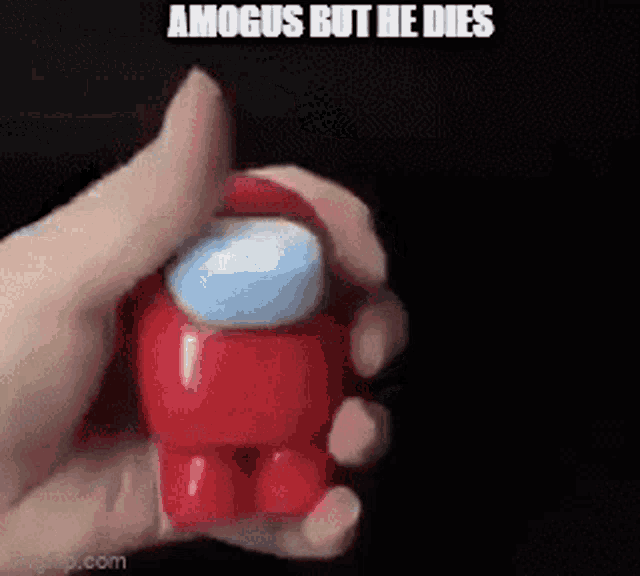 a person is holding a red among us toy in their hand with a black background .