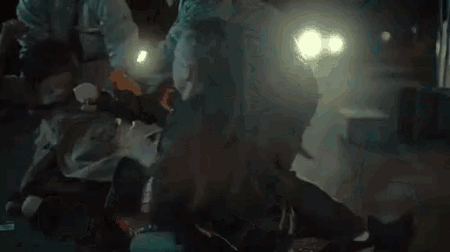 a group of people are standing around a man laying on the ground in the dark .