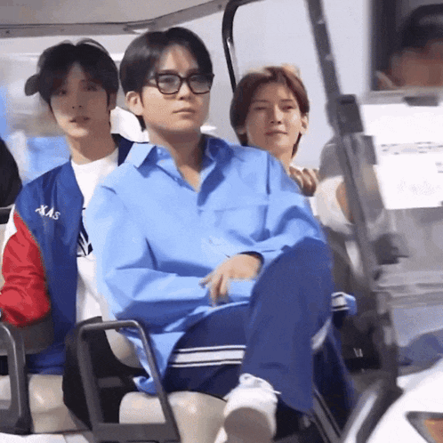 a man in a blue shirt is sitting in a golf cart with other people
