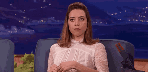 a woman in a white dress is sitting in a chair and making a face .