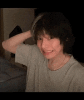 a young man with short hair is smiling and holding his hair in a room .