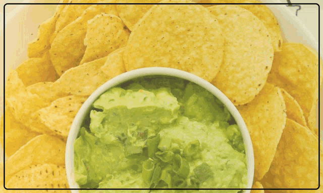 a bowl of guacamole sits on top of a pile of tortilla chips