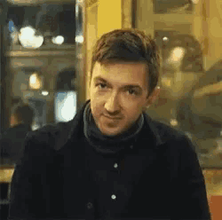 a man in a black jacket is making a funny face in front of a window .