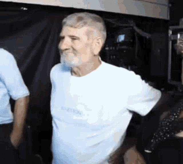 a man with a beard wearing a white t-shirt is dancing in a dark room .