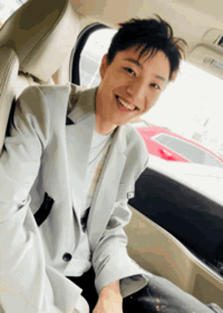 a man in a grey jacket is smiling while sitting in a car