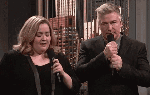 a woman is singing into a microphone next to a man in a suit .